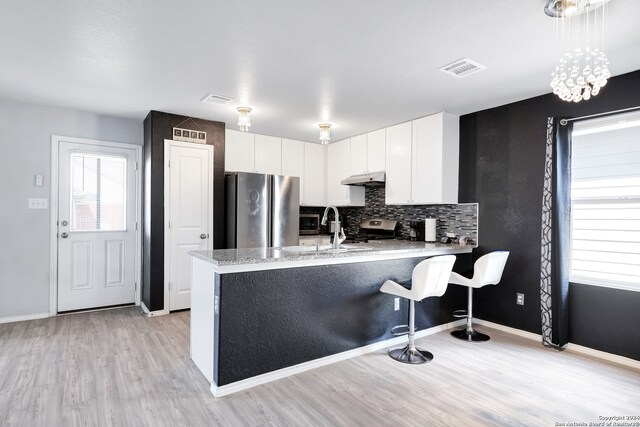 kitchen featuring white cabinets, hanging light fixtures, appliances with stainless steel finishes, light hardwood / wood-style floors, and kitchen peninsula