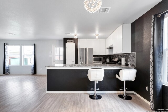 kitchen featuring white cabinets, light hardwood / wood-style flooring, decorative backsplash, appliances with stainless steel finishes, and kitchen peninsula