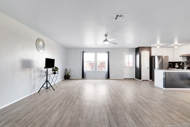 unfurnished living room featuring light wood-type flooring, ceiling fan, and sink