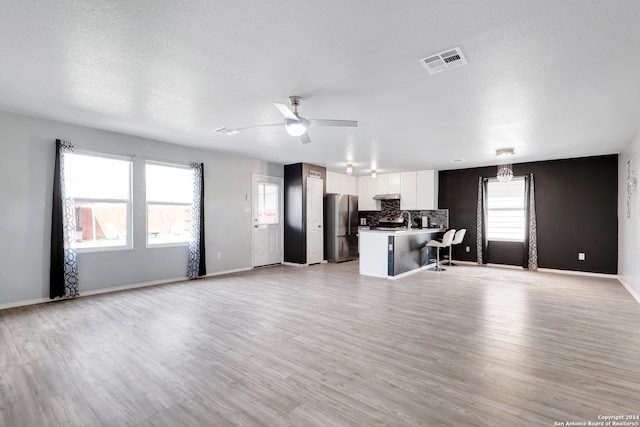 living room featuring ceiling fan, a textured ceiling, a wealth of natural light, and light hardwood / wood-style flooring