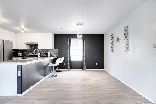 kitchen with kitchen peninsula, white cabinetry, stainless steel appliances, and light hardwood / wood-style flooring