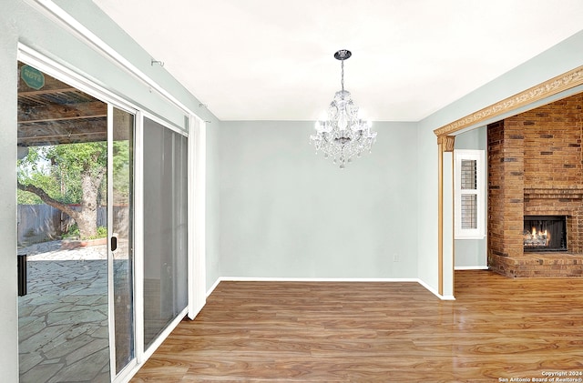 unfurnished dining area with a chandelier, a fireplace, and wood-type flooring