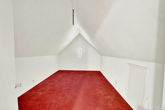 bonus room with a textured ceiling, dark colored carpet, and lofted ceiling