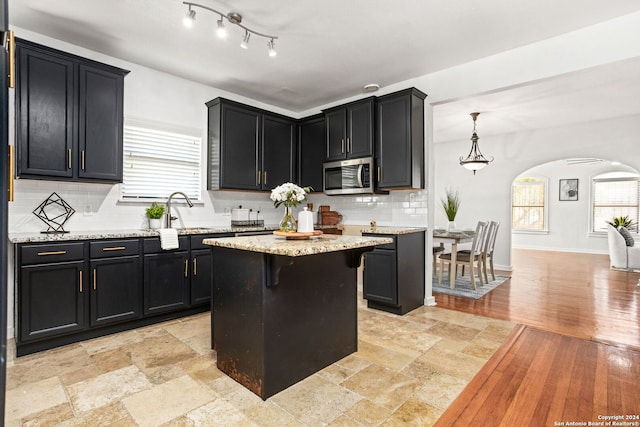 kitchen with light hardwood / wood-style flooring, decorative light fixtures, a kitchen island, sink, and decorative backsplash