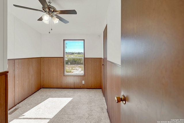 empty room featuring light colored carpet, wooden walls, and ceiling fan