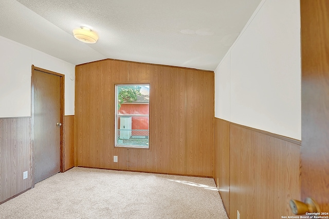 unfurnished room featuring crown molding, a textured ceiling, wooden walls, and lofted ceiling