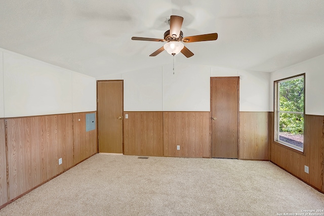 spare room featuring light carpet, lofted ceiling, ceiling fan, and wooden walls