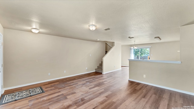 empty room with a textured ceiling, hardwood / wood-style floors, and a notable chandelier