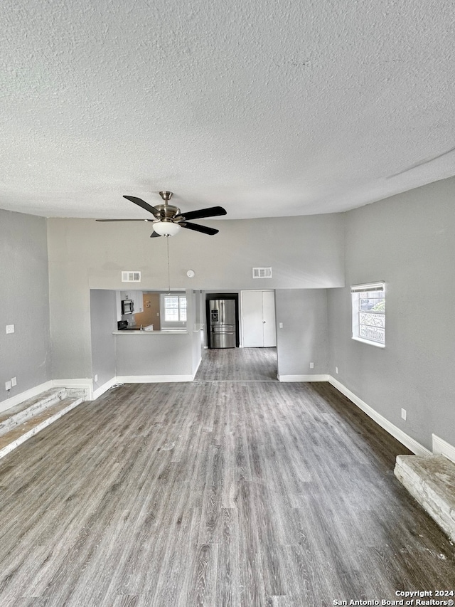 unfurnished living room featuring ceiling fan, hardwood / wood-style flooring, plenty of natural light, and a textured ceiling