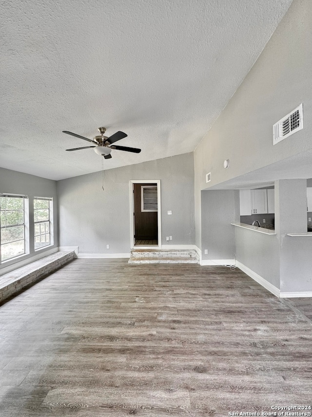 unfurnished living room featuring vaulted ceiling, a textured ceiling, light hardwood / wood-style flooring, and ceiling fan