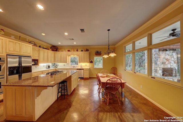 kitchen with a center island, a breakfast bar, ornamental molding, stainless steel appliances, and ceiling fan