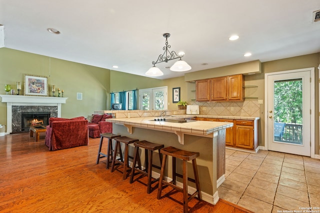 kitchen featuring tile countertops, a kitchen bar, a premium fireplace, hanging light fixtures, and light hardwood / wood-style floors