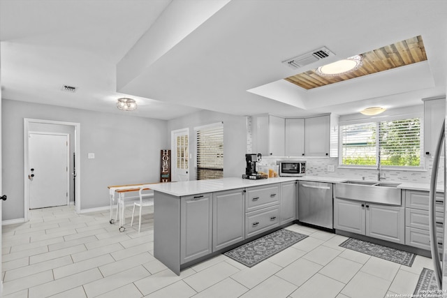 kitchen featuring stainless steel appliances, sink, a raised ceiling, kitchen peninsula, and tasteful backsplash