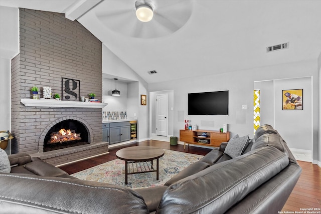 living room featuring a brick fireplace, hardwood / wood-style floors, beverage cooler, ceiling fan, and beam ceiling