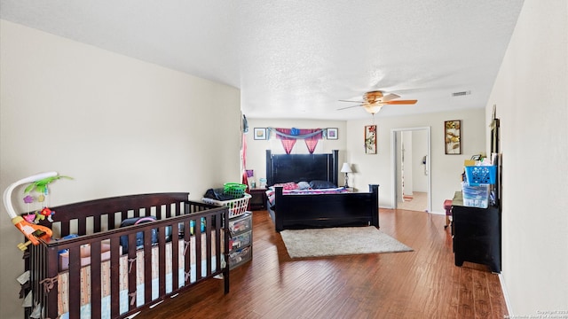 bedroom featuring hardwood / wood-style flooring, ceiling fan, a textured ceiling, and a nursery area