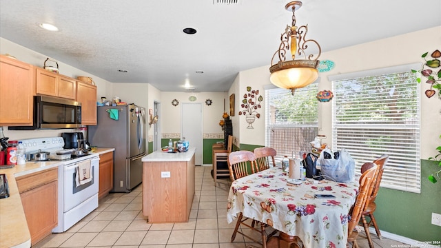 kitchen with light tile patterned floors, pendant lighting, light brown cabinetry, a kitchen island, and appliances with stainless steel finishes