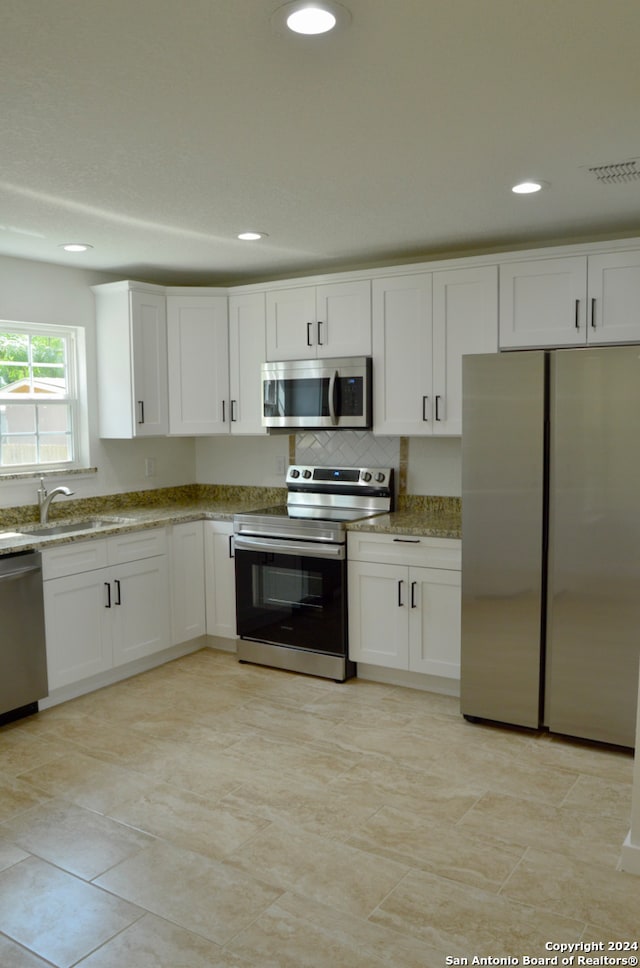 kitchen featuring light stone counters, sink, decorative backsplash, appliances with stainless steel finishes, and white cabinets