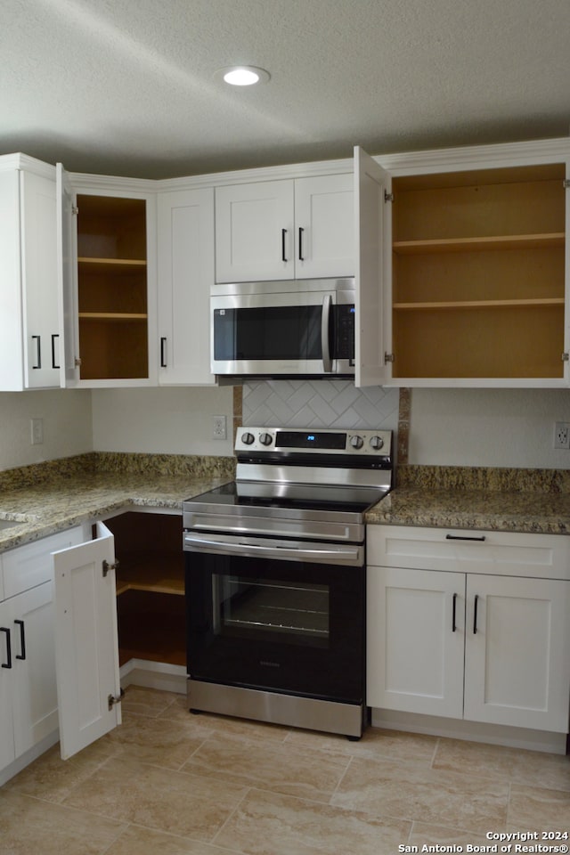 kitchen featuring a textured ceiling, light stone counters, appliances with stainless steel finishes, and white cabinets