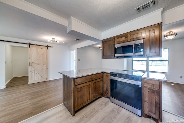 kitchen featuring stainless steel appliances, ornamental molding, kitchen peninsula, a barn door, and light wood-type flooring