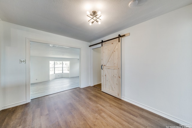 unfurnished bedroom featuring a textured ceiling, a barn door, and light hardwood / wood-style floors