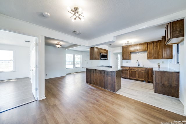 kitchen with stovetop, a textured ceiling, sink, and light hardwood / wood-style floors