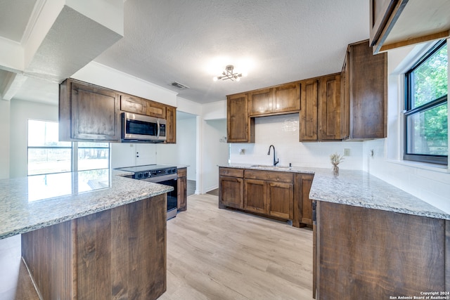 kitchen with light wood-type flooring, appliances with stainless steel finishes, light stone counters, and decorative backsplash