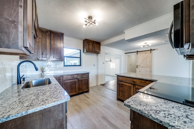 kitchen with a barn door, light stone countertops, sink, and light hardwood / wood-style flooring