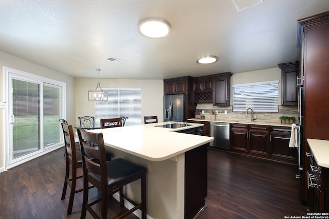 kitchen featuring dark hardwood / wood-style flooring, a center island, decorative backsplash, pendant lighting, and appliances with stainless steel finishes