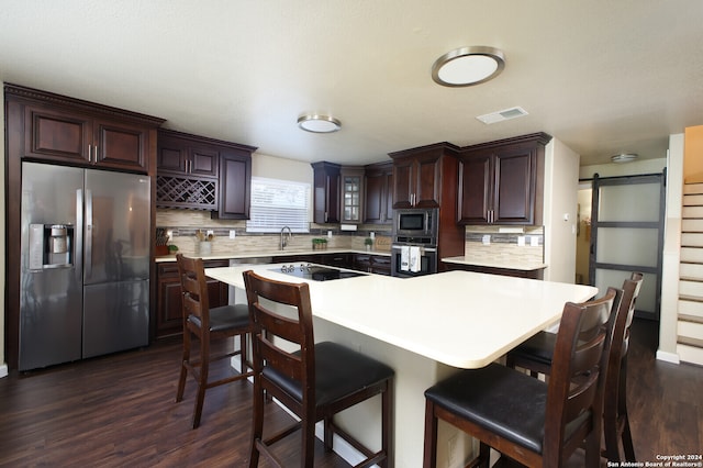 kitchen featuring decorative backsplash, a barn door, dark hardwood / wood-style floors, and stainless steel appliances