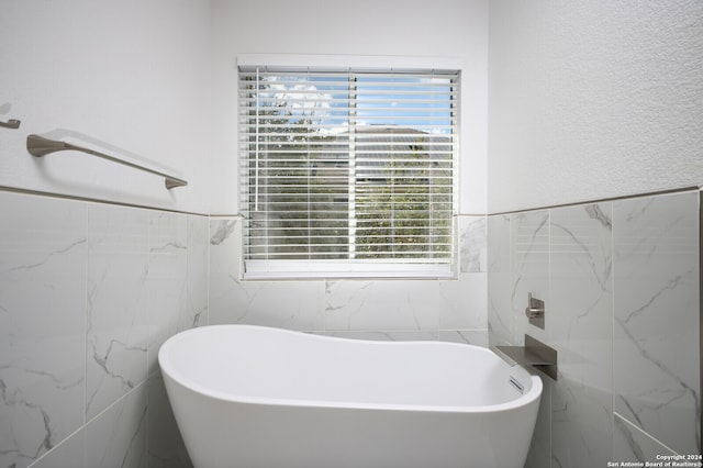 bathroom with tile walls, a wealth of natural light, and a tub