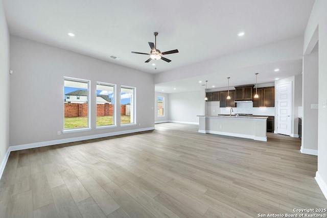 unfurnished living room with ceiling fan, sink, and light wood-type flooring