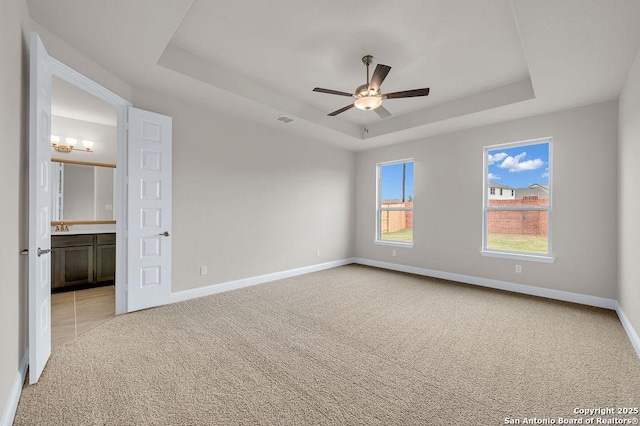 spare room featuring a raised ceiling, light carpet, and ceiling fan