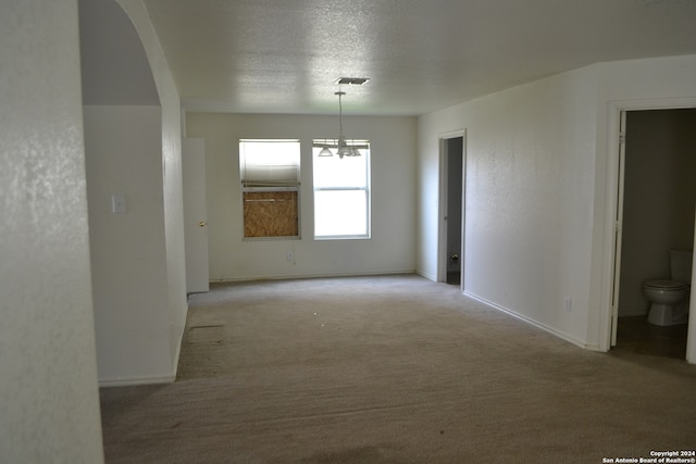 carpeted spare room with a textured ceiling and a notable chandelier