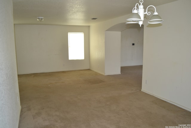 spare room featuring a textured ceiling, light colored carpet, and an inviting chandelier