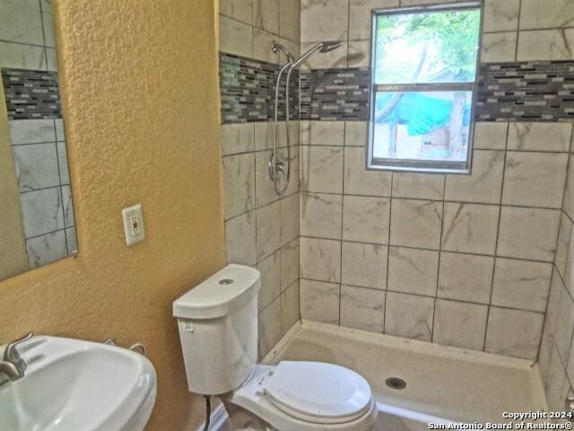 bathroom featuring a shower stall, toilet, a textured wall, and a sink