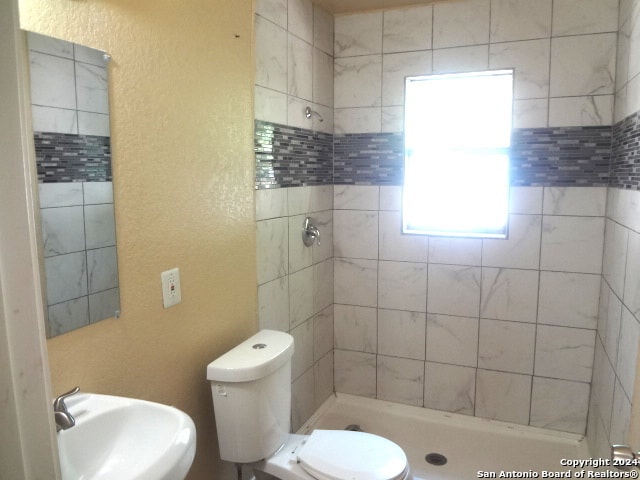 bathroom featuring tiled shower, toilet, and sink