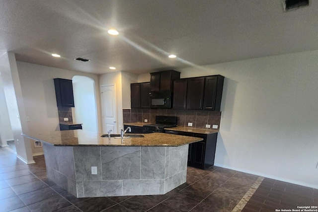 kitchen featuring light stone countertops, sink, black appliances, and an island with sink