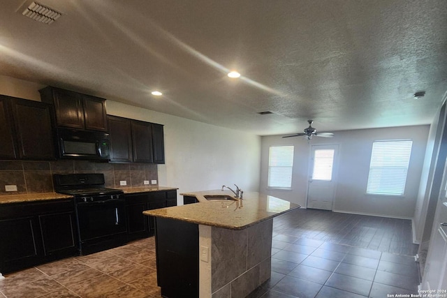 kitchen featuring decorative backsplash, ceiling fan, black appliances, a center island with sink, and light hardwood / wood-style flooring