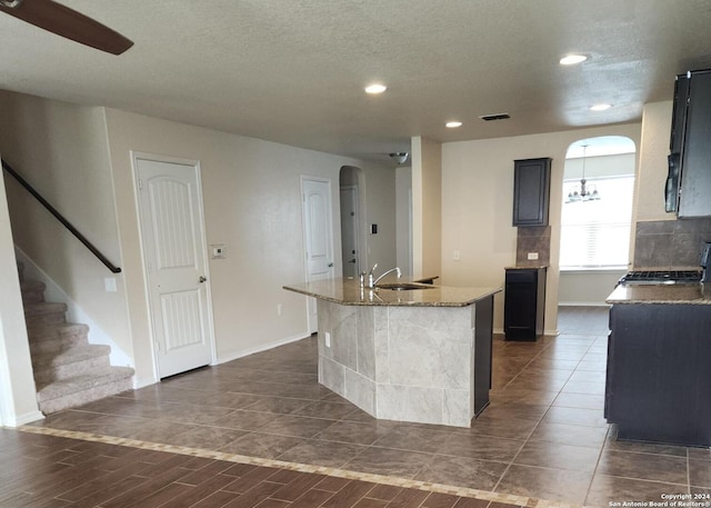 kitchen featuring dark hardwood / wood-style flooring, light stone counters, a textured ceiling, sink, and an island with sink