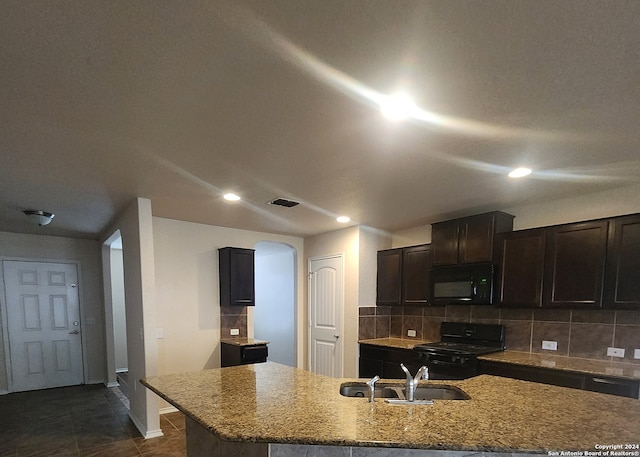 kitchen with sink, light stone counters, backsplash, an island with sink, and black appliances