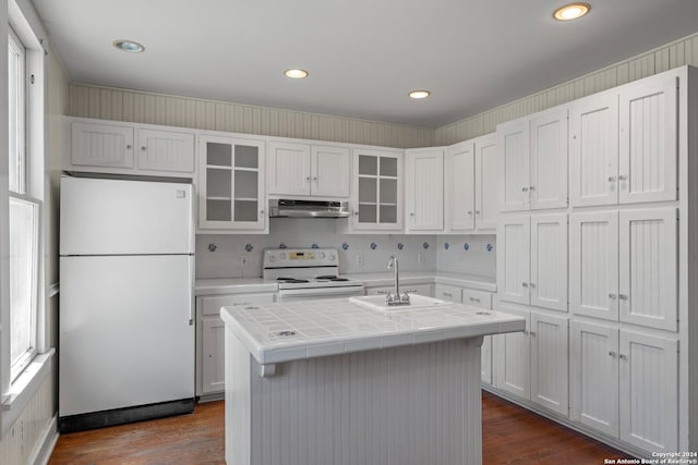 kitchen with white appliances, a wealth of natural light, tile counters, and a center island with sink