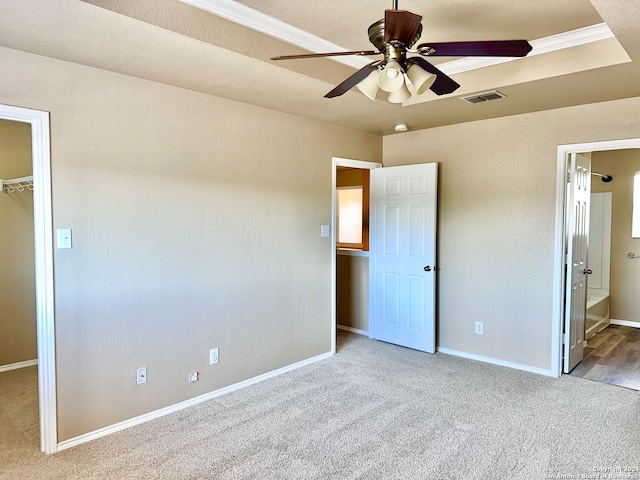 unfurnished bedroom with ceiling fan, connected bathroom, a walk in closet, a closet, and light colored carpet