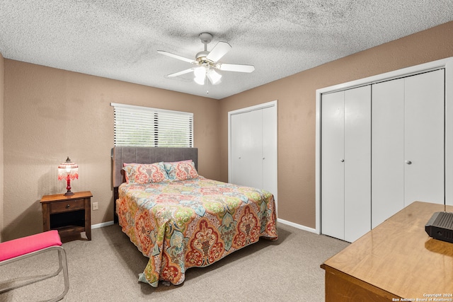 bedroom featuring a textured ceiling, light colored carpet, ceiling fan, and multiple closets