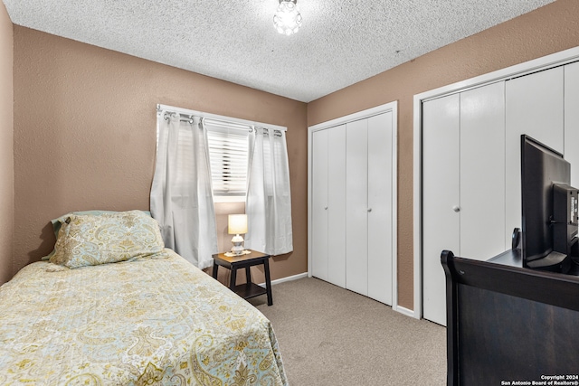 carpeted bedroom featuring a textured ceiling and two closets