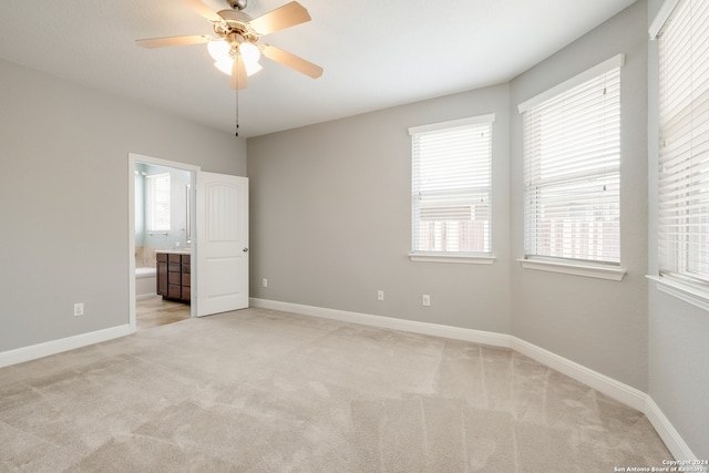 unfurnished bedroom featuring ensuite bath, light colored carpet, and ceiling fan