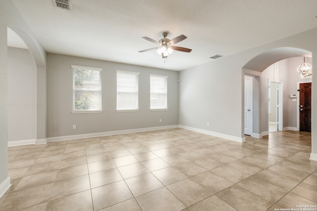 tiled empty room with a textured ceiling and ceiling fan with notable chandelier