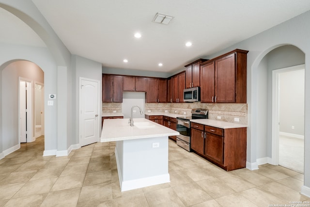 kitchen featuring an island with sink, backsplash, sink, and appliances with stainless steel finishes