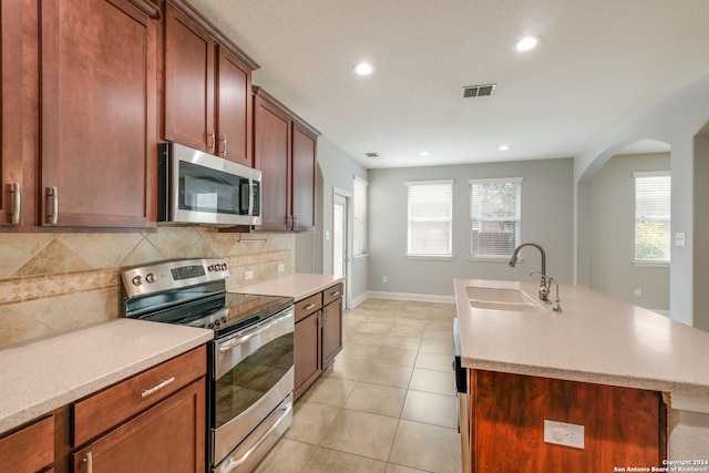 kitchen featuring appliances with stainless steel finishes, a kitchen island with sink, sink, decorative backsplash, and light tile patterned flooring