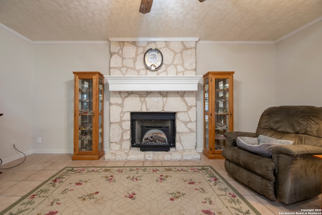 living room with ceiling fan, a stone fireplace, ornamental molding, and light tile patterned floors