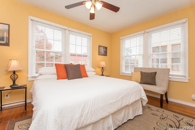 bedroom with a baseboard heating unit, multiple windows, hardwood / wood-style floors, and ceiling fan